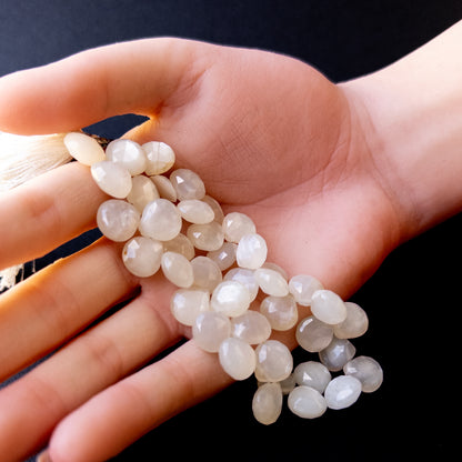 A person holds delicate strands of White Rainbow Moonstone beads, showcasing their faceted briolette design.