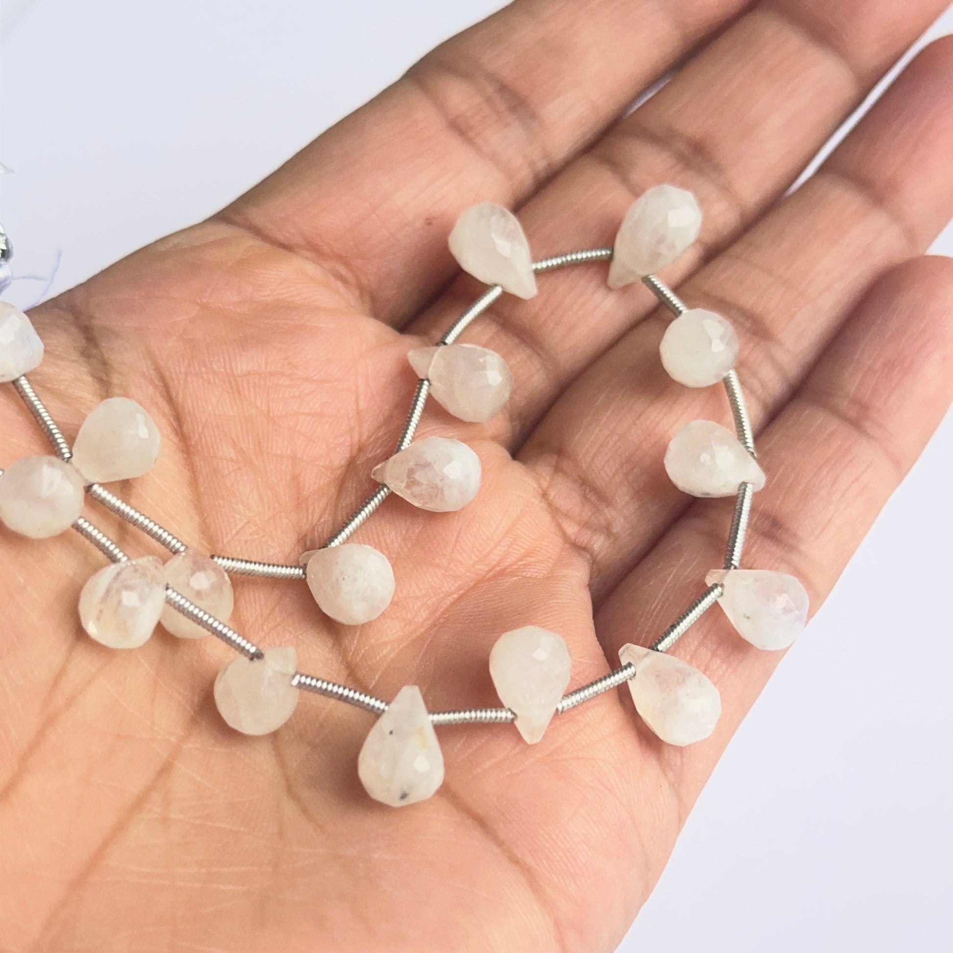 A person holds delicate strands of rainbow moonstone beads, showcasing their smooth design.