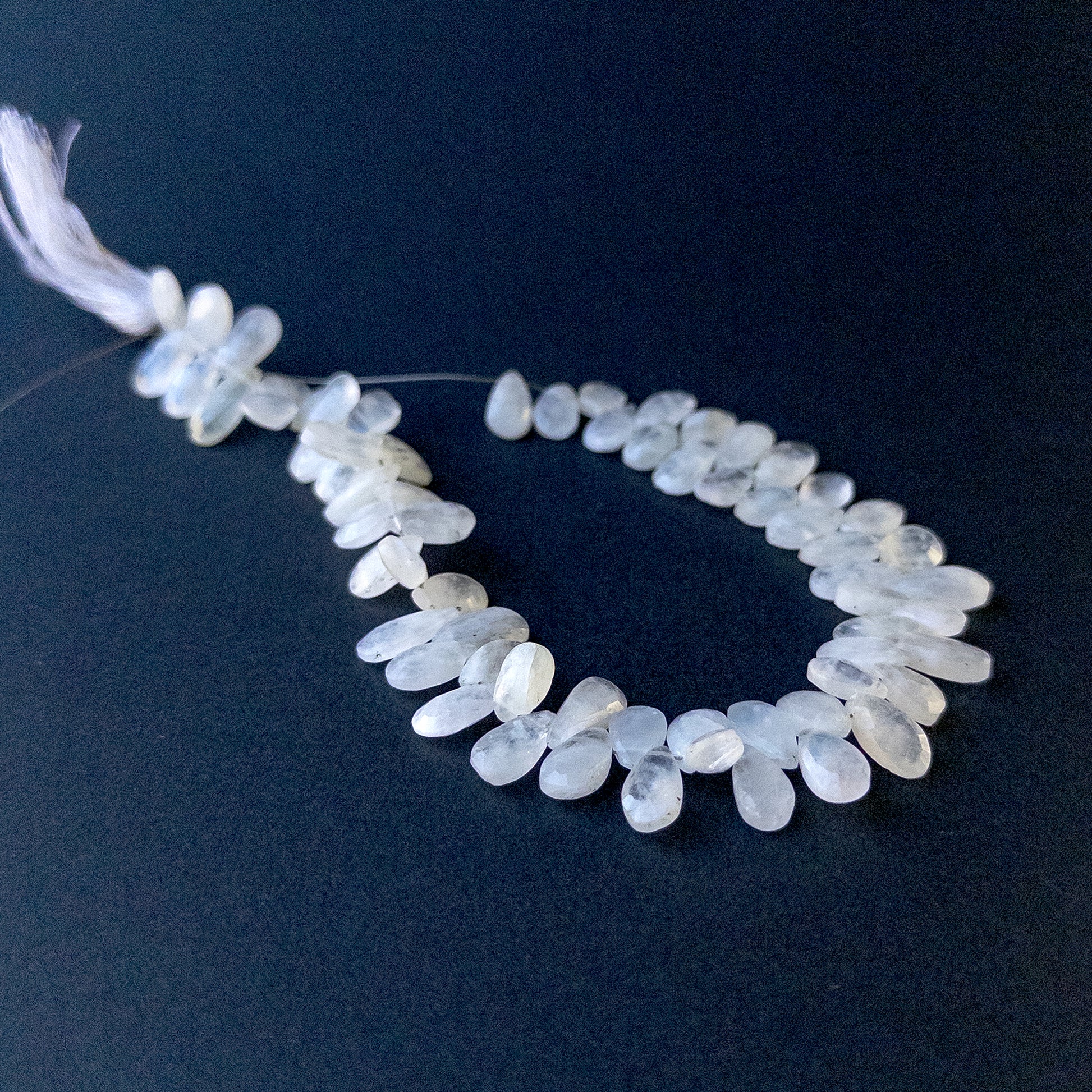 Close‑up of Rainbow Moonstone faceted briolette pear beads showing iridescent shimmer and polished facets.