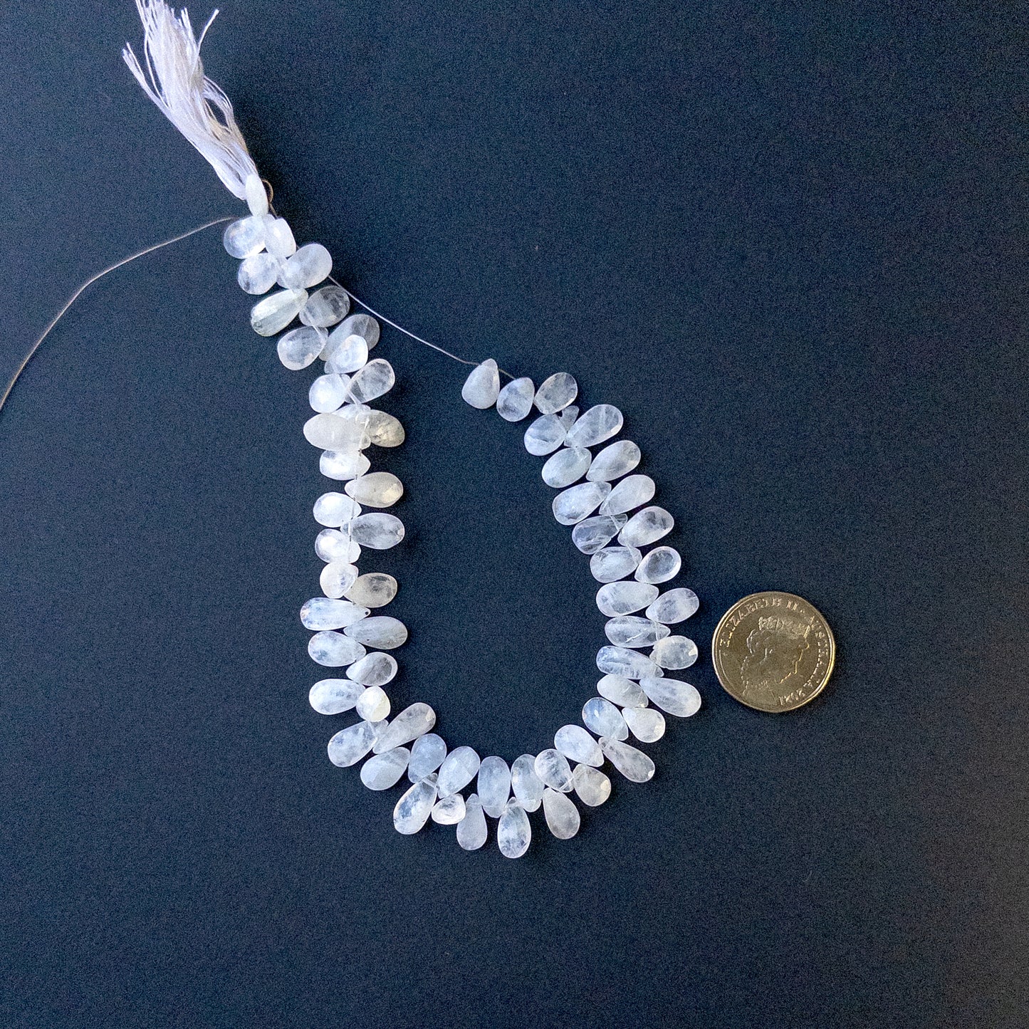 A coin is placed near delicate strands of White Rainbow Moonstone faceted briolette pear beads for scale.