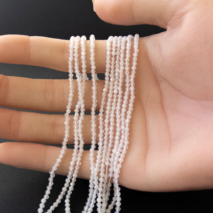 A person holds delicate strands of White Rainbow Moonstone beads, showcasing their faceted rondelle design.