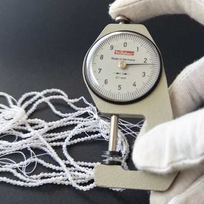 A dial gauge measures the White Rainbow Moonstone faceted rondelle 2.3–2.4mm gemstone.