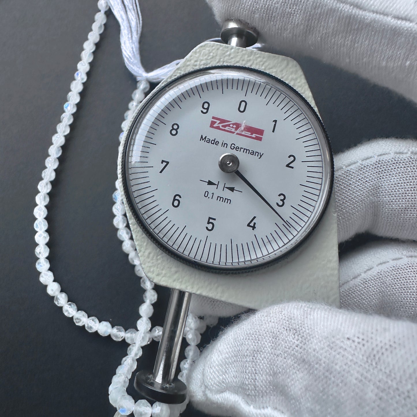 A dial gauge measures the White Rainbow Moonstone faceted rondelle 3.3-3.4mm gemstone.