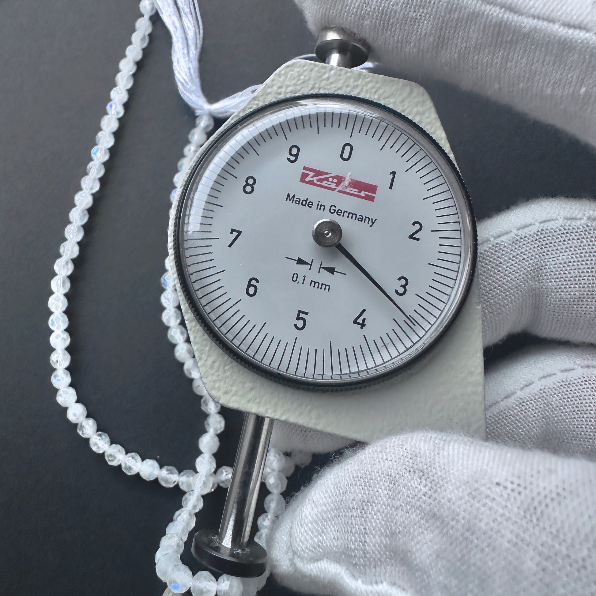 A dial gauge measures the White Rainbow Moonstone faceted rondelle 3.3-3.4mm gemstone.