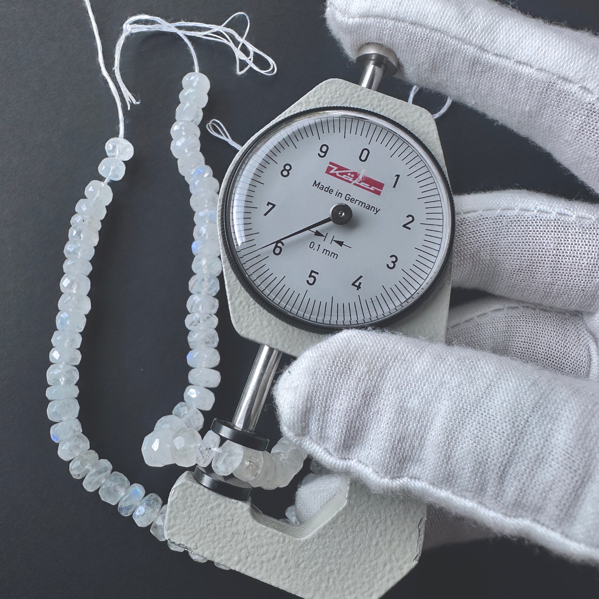 A dial gauge measures the White Rainbow Moonstone faceted rondelle 6.2mm gemstone.