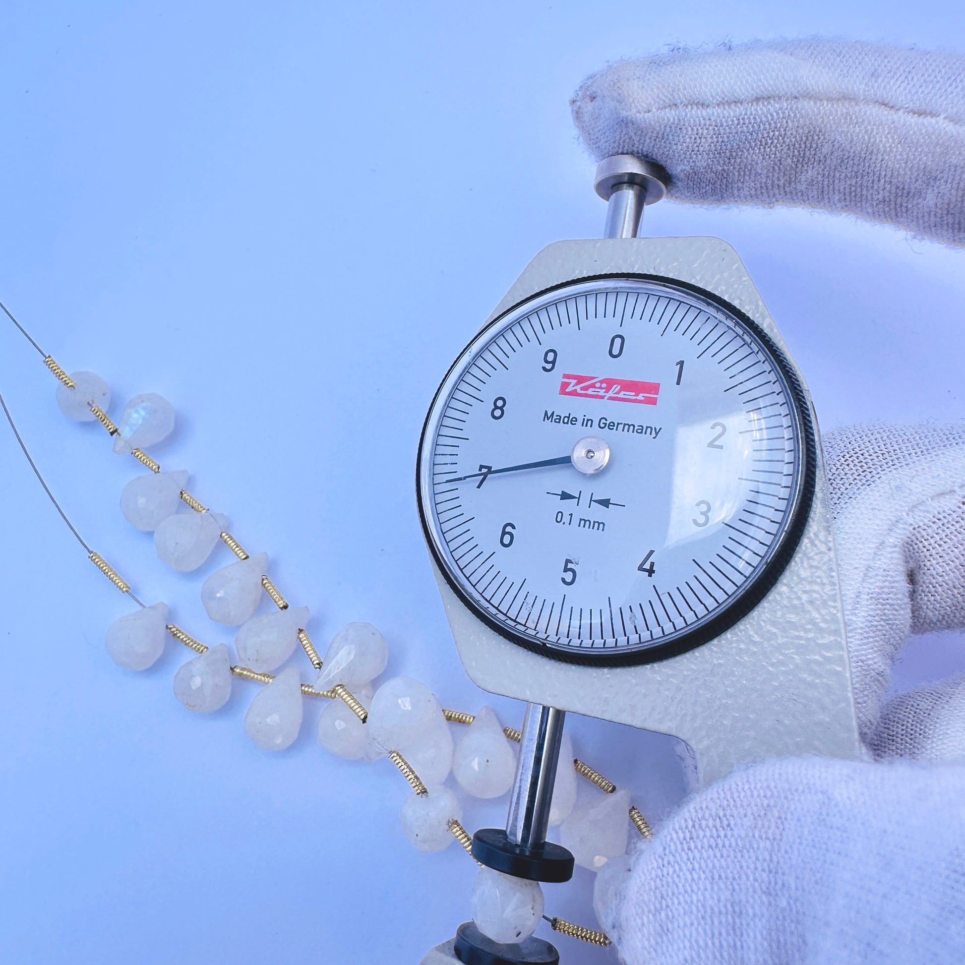 A dial gauge measures the White Rainbow Moonstone faceted teardrop 4.1–11.5mm gemstone.