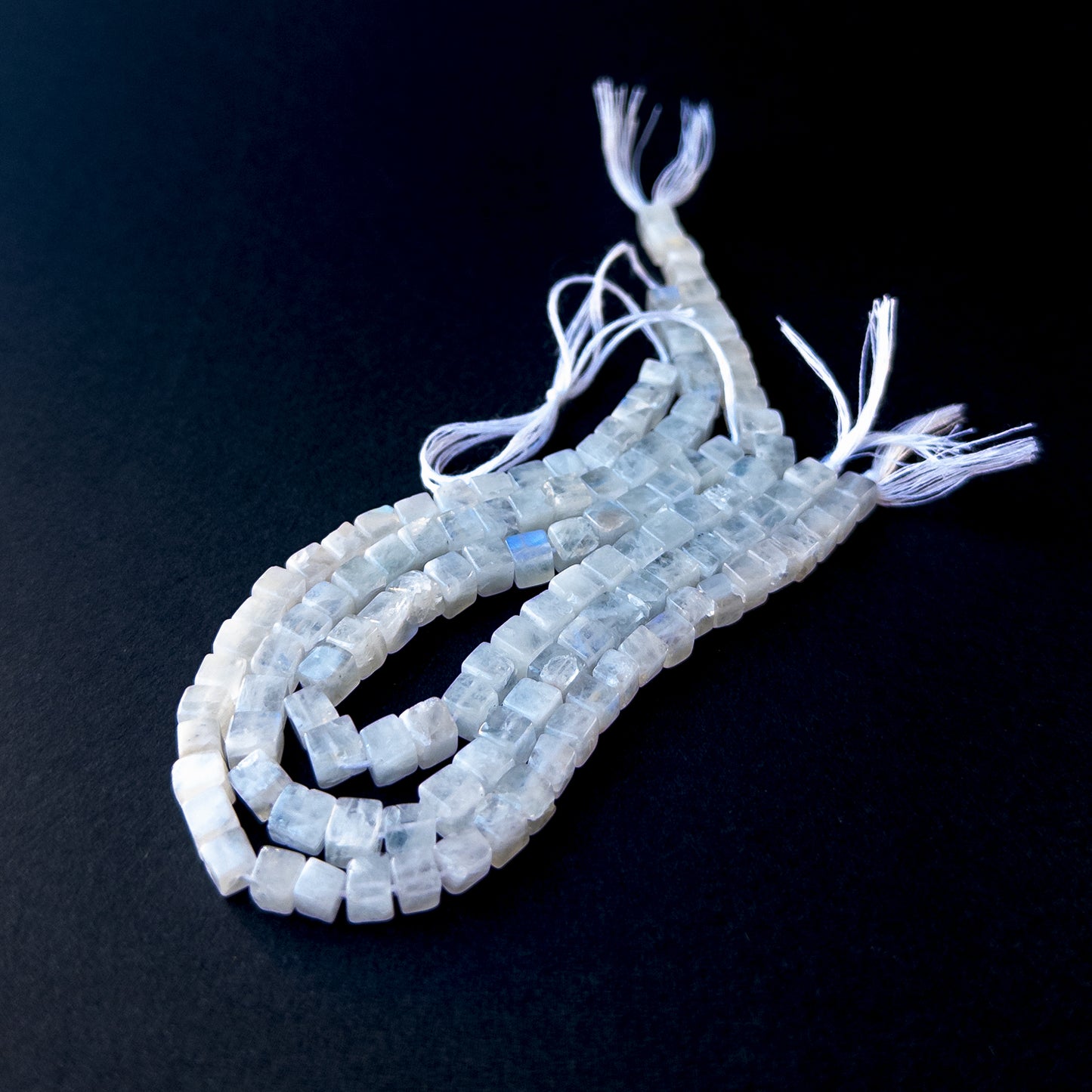 Premium Moonstone smooth cube beads arranged neatly on a short strand with glowing white‑blue colour.