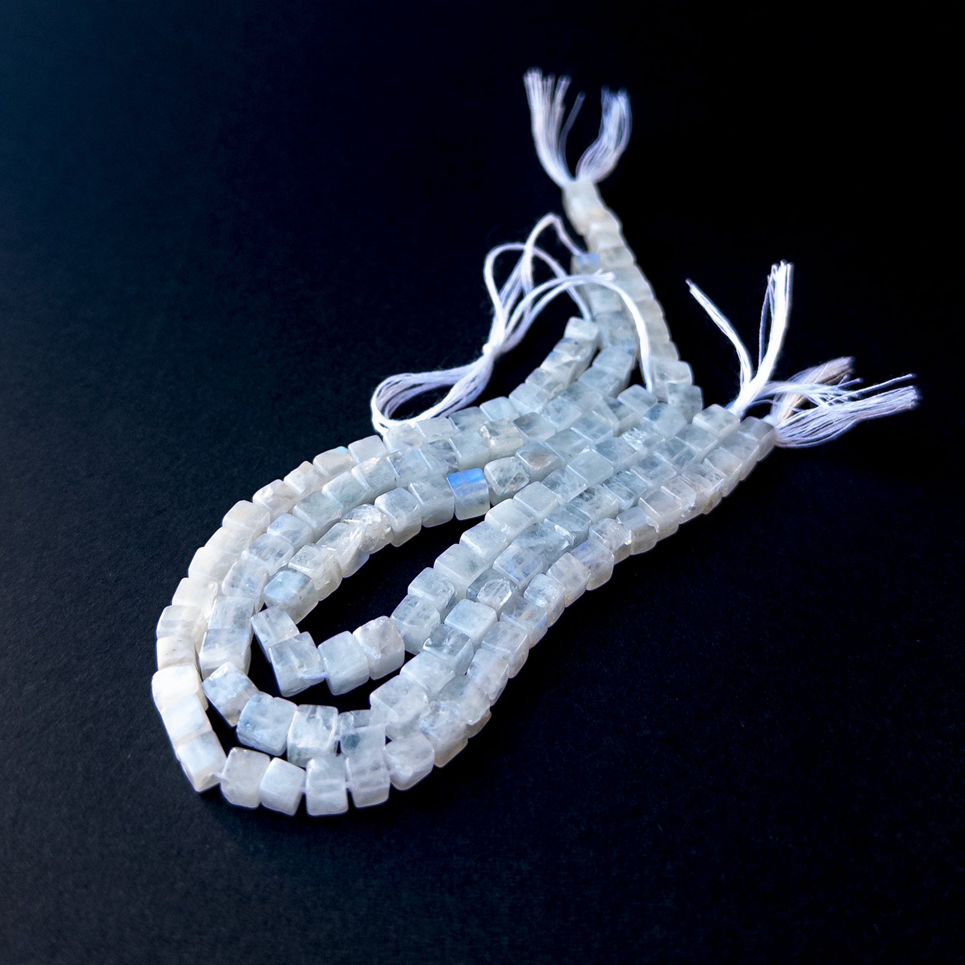 Premium Moonstone smooth cube beads arranged neatly on a short strand with glowing white‑blue colour.