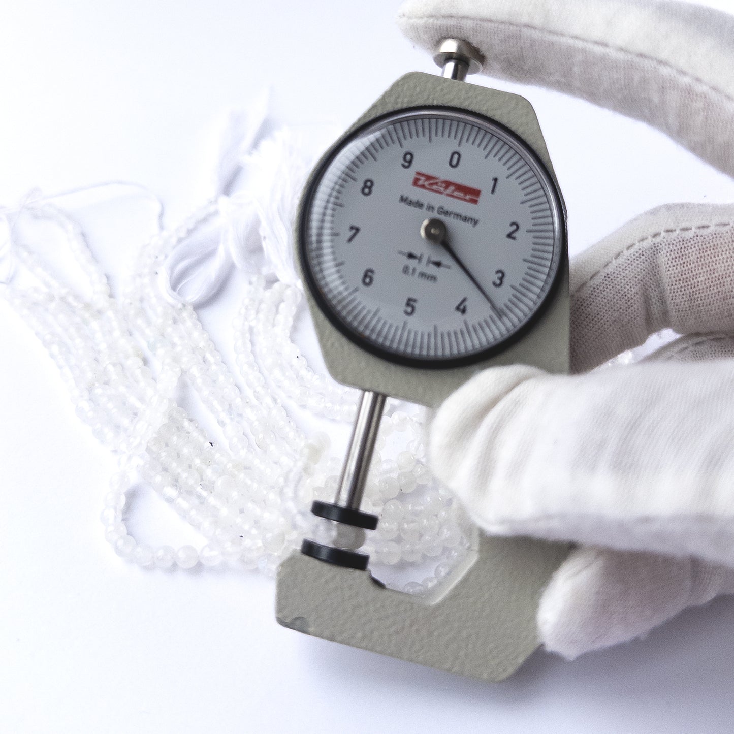 A dial gauge measures the White Rainbow Moonstone smooth round 3.5mm gemstone.