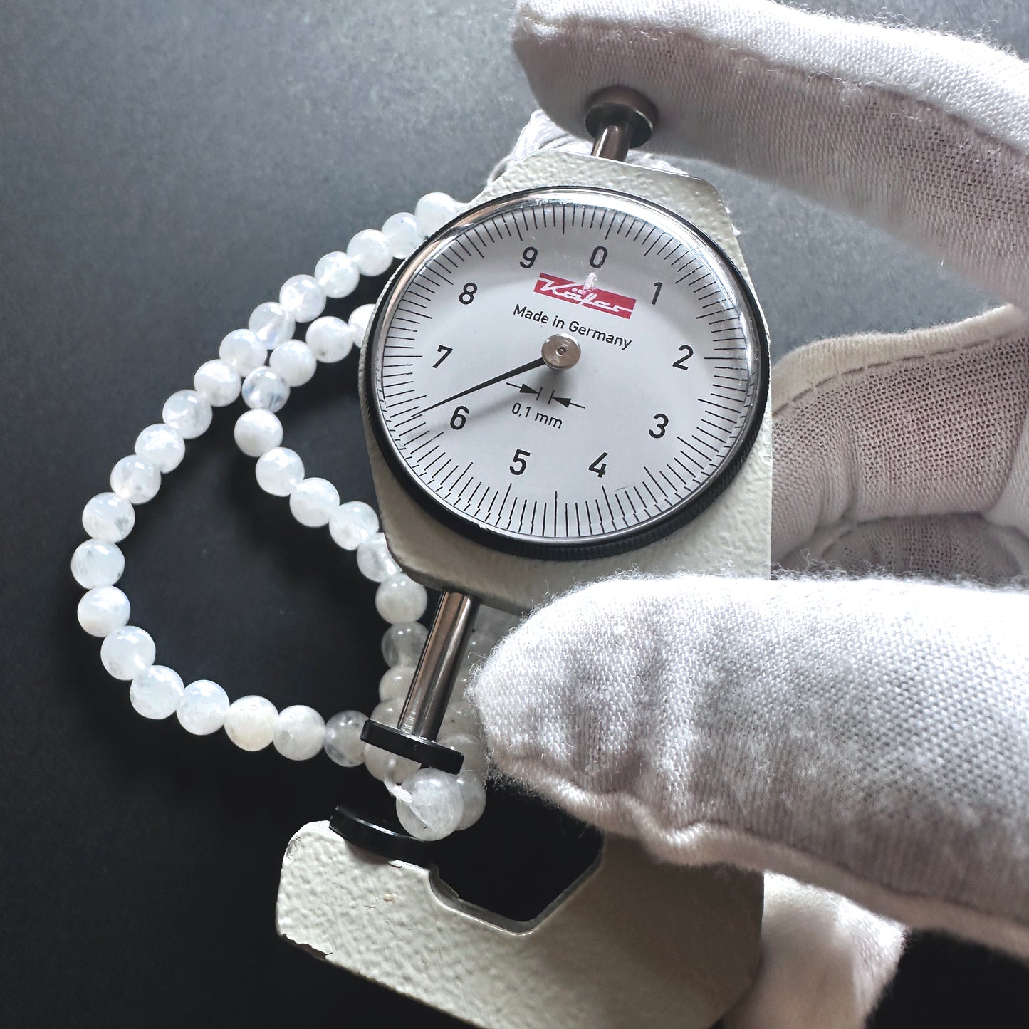 A dial gauge measures the White Rainbow Moonstone smooth round 6-6.5mm gemstone.
