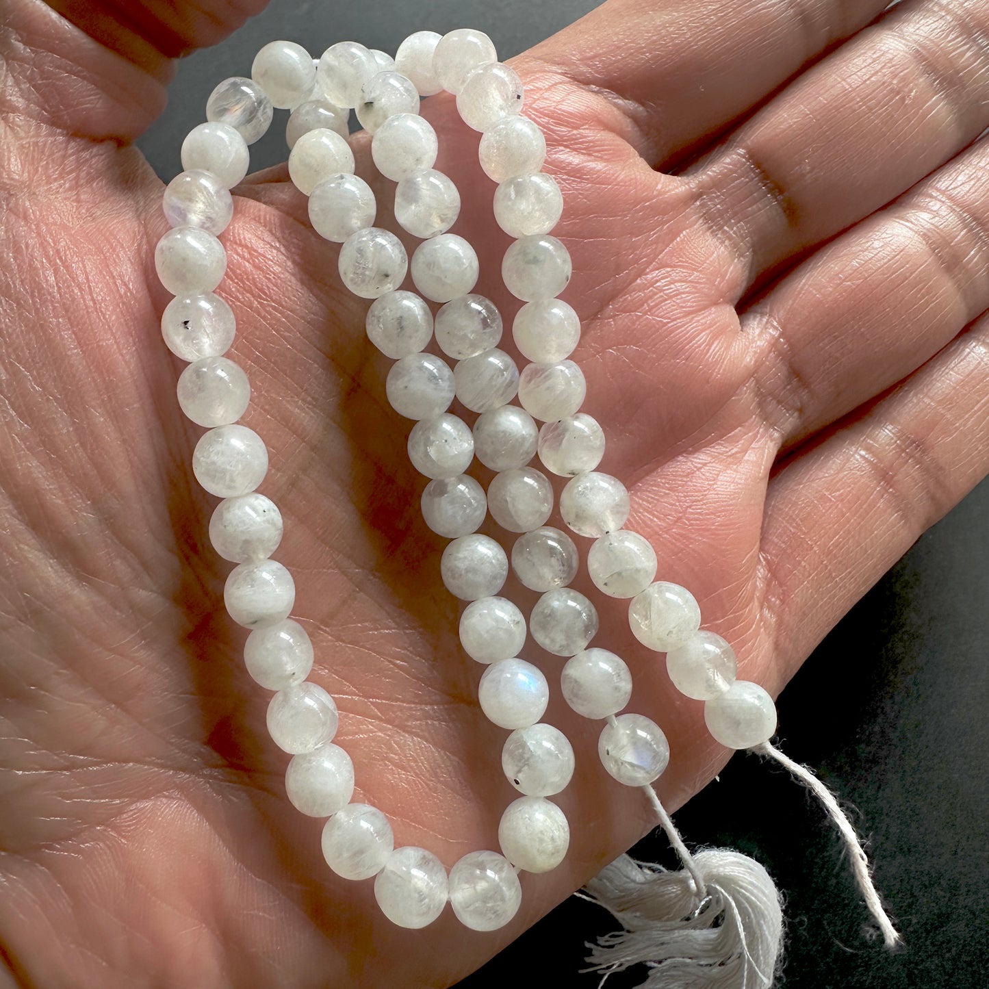 A person holds delicate strands of White Rainbow Moonstone beads, showcasing their smooth design.