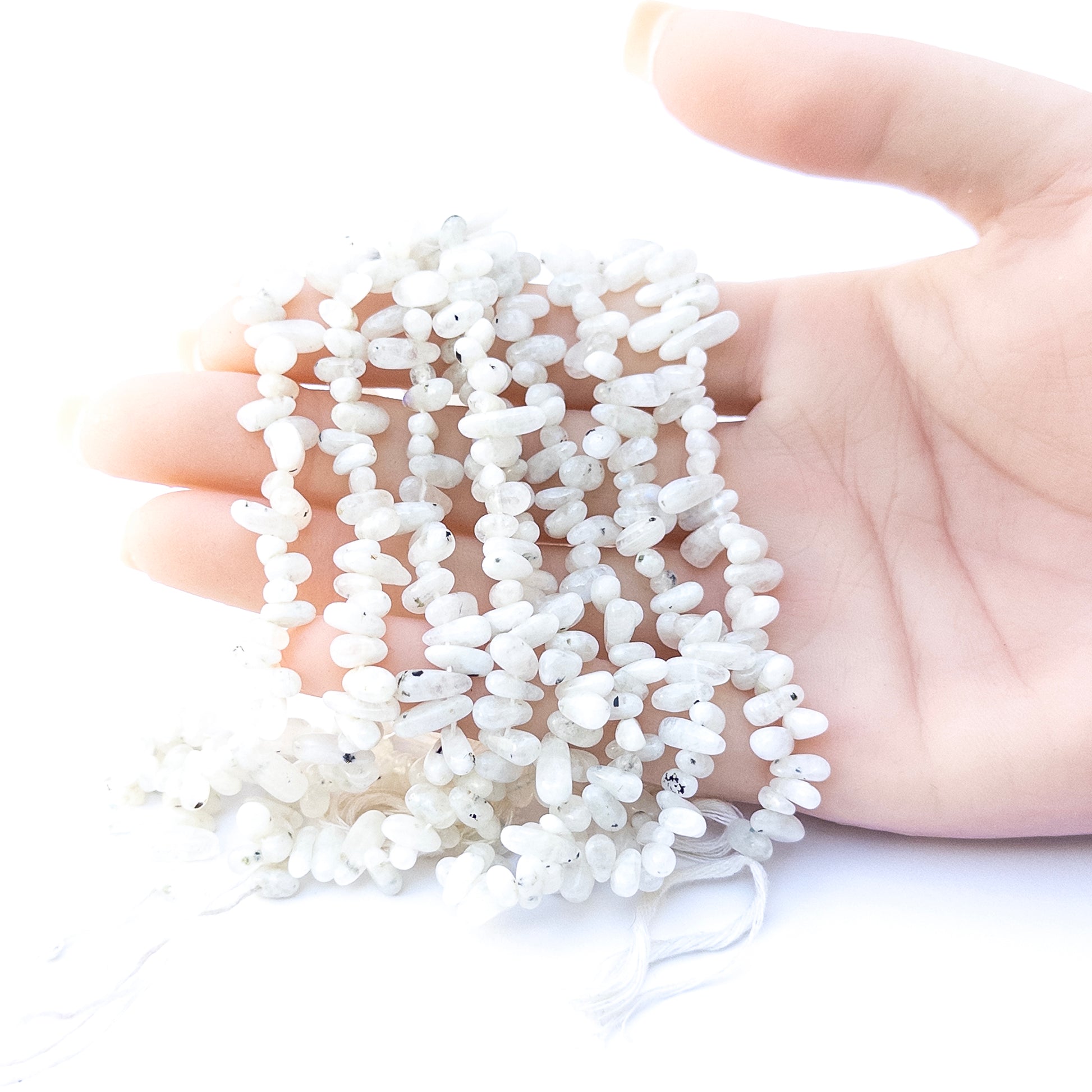 A person holds delicate strands of White Rainbow beads, showcasing their smooth nugget design.