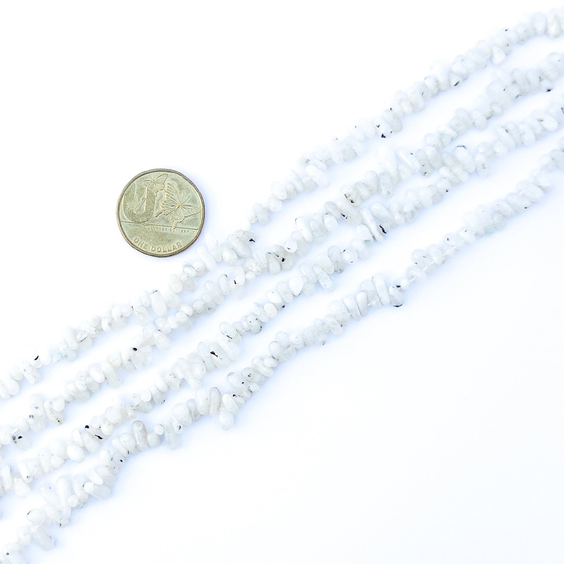 A coin is place near delicate strands of White Rainbow beads for scale