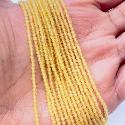 A person holds delicate strands of yellow chalcedony beads, showcasing their faceted design.