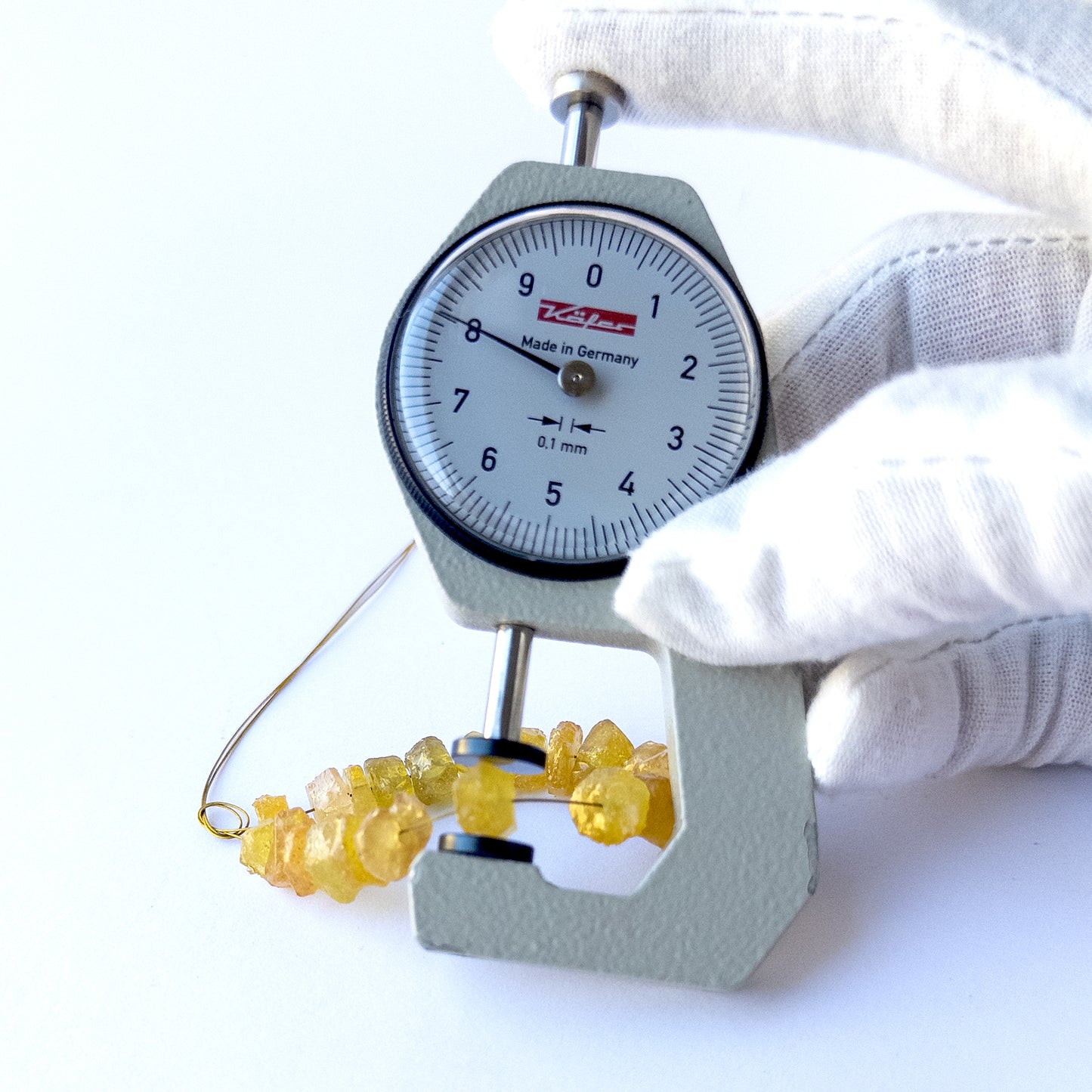 A dial gauge measures the Yellow Sapphire drilled rough 7–9mm gemstone.