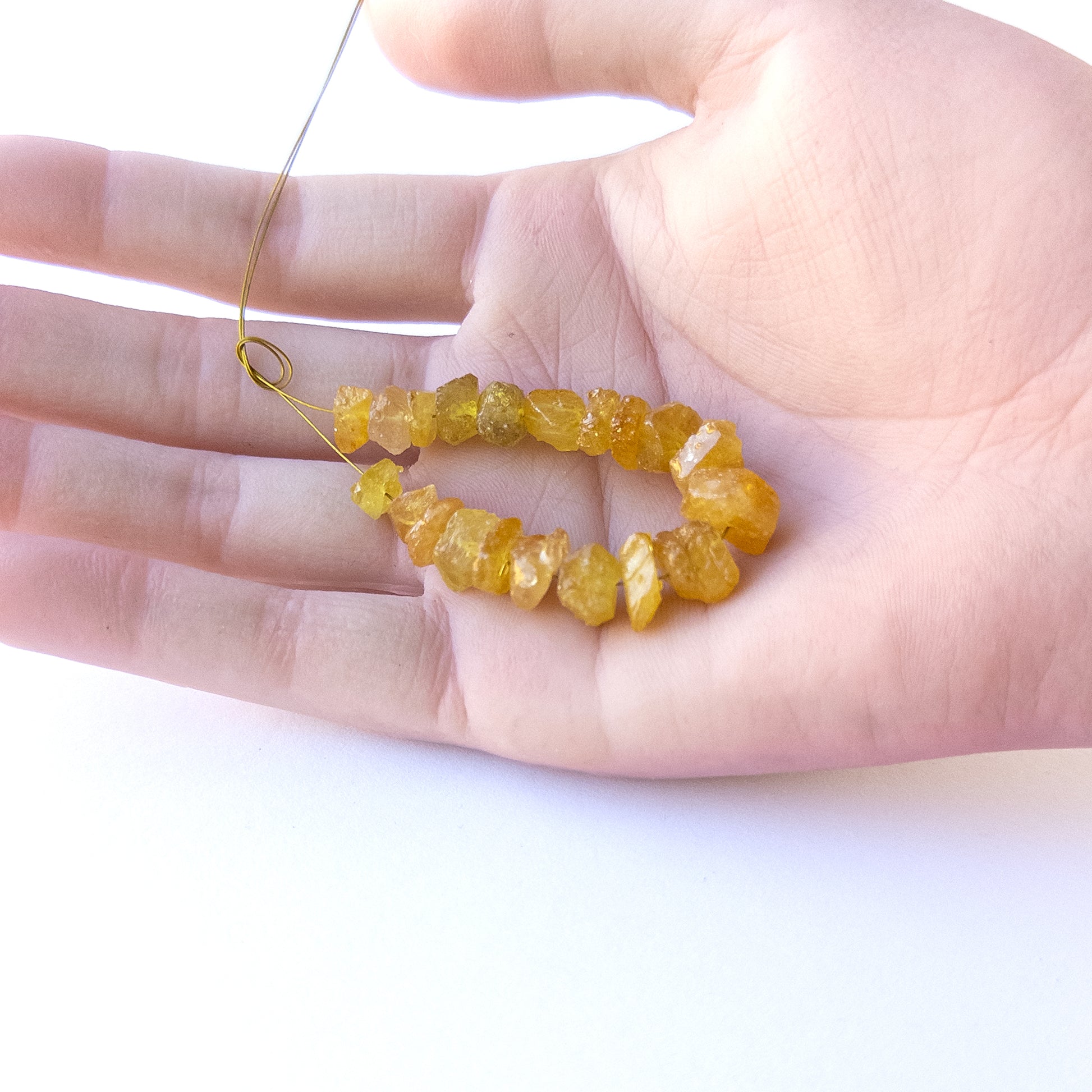 A person holds delicate pieces of Yellow Sapphire rough beads, showcasing their drilled rough design.