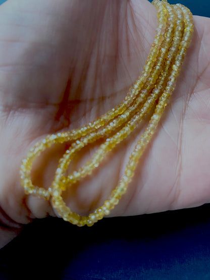 A person holds delicate strands of Yellow Sapphire beads, showcasing their colour and faceted design.