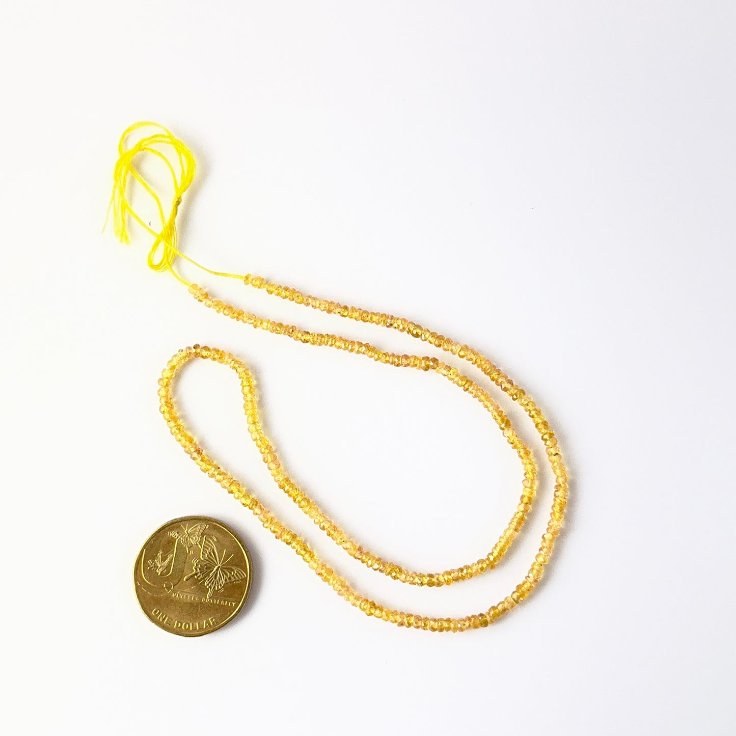 A coin is placed near delicate strands of Yellow Sapphire beads for scale.