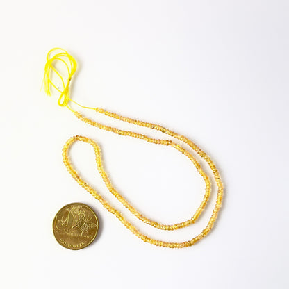 A coin is placed near delicate strands of Yellow Sapphire beads for scale.