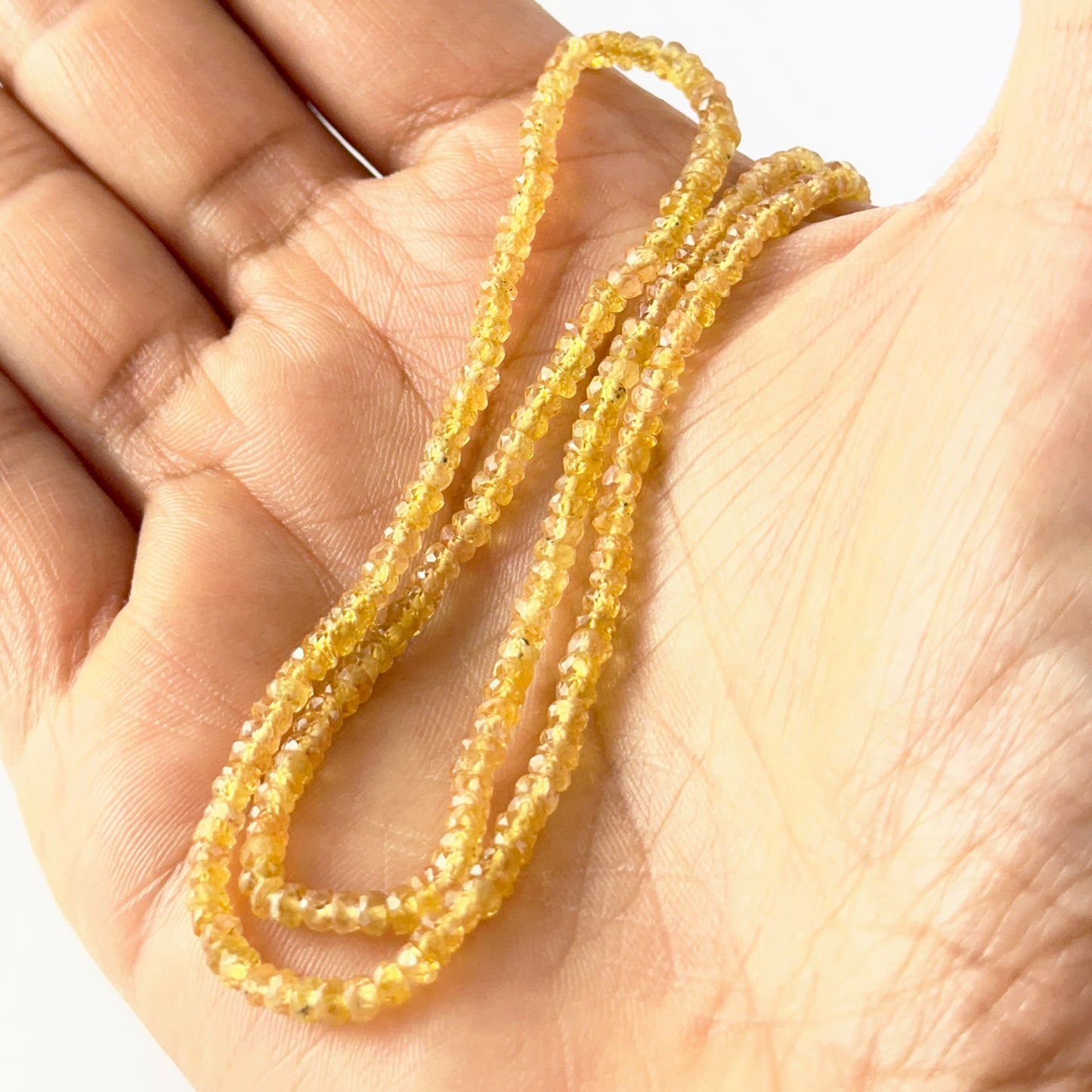 A person holds delicate strands of Yellow Sapphire beads, showcasing their faceted rondelle design.
